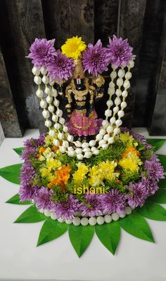 there is a statue made out of flowers and beads on top of a table with green leaves