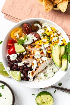 a white bowl filled with chicken, black beans, corn and avocado next to tortilla chips