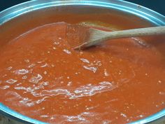 a wooden spoon in a metal pan filled with tomato sauce