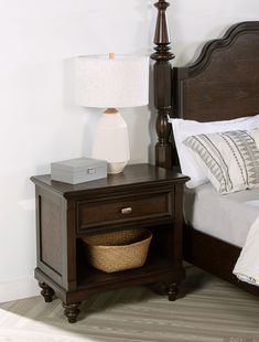 a night stand with a basket underneath it and a lamp on the nightstand next to it