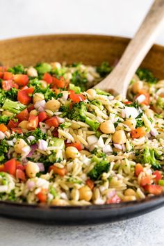 broccoli and other vegetables are mixed together in a skillet with a wooden spoon