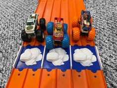 three toy trucks are on an orange track