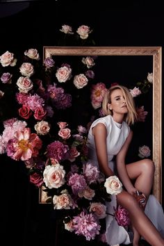 a woman sitting in front of a painting surrounded by flowers