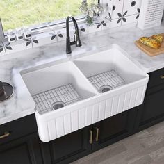 a double white kitchen sink sitting on top of a counter next to a wooden cutting board