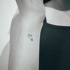 a woman's arm with a small heart and arrow tattoo on the left wrist