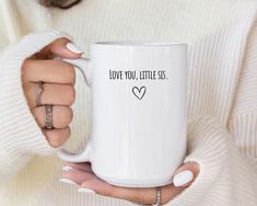 a woman holding a coffee mug with the words love you, little sis on it