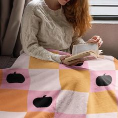 a woman reading a book while sitting on a bed with an apple blanket over her