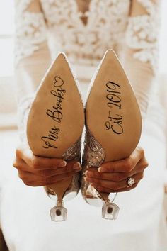 two brides holding their shoes with the names of their wedding day written on them