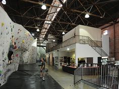 two people climbing up the side of a rock wall in an indoor climbing area with stairs and railings