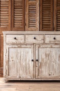 an old white wooden cabinet with shutters on the wall and wood flooring behind it