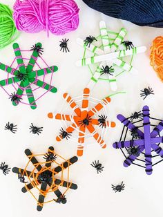 several spider webs and balls of yarn on a white surface with orange, green, purple, and black pins