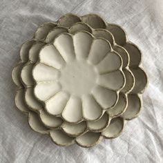 a white flower dish sitting on top of a cloth covered tablecloth with the edge of it's bowl