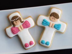 two decorated cookies are sitting on a white plate with blue and pink icing, one is shaped like a cross