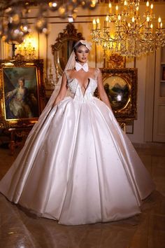 a woman in a white wedding dress standing next to a chandelier and paintings