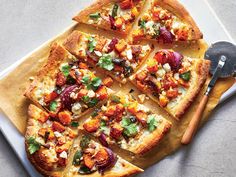 a pizza with many toppings cut into slices on a cutting board next to a spatula