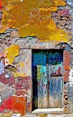 an old door is painted on the side of a stone building with peeling paint and rust