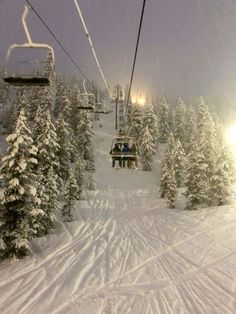 a ski lift is going up the snowy mountain side with trees in front of it