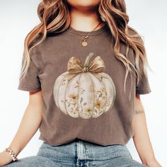 Fall Coquette Pumpkin with Bow Comfort Colors Shirt Embrace the cozy vibes of Fall with our Comfort Colors tee featuring a charming Coquette Pumpkin adorned with a delicate bow. The soft autumn hues of Yam, mustard, espresso, ivory, bay, and brick beautifully capture the essence of the season, making this shirt perfect for Fall, Halloween, and Thanksgiving celebrations. Crafted from 100% ring-spun US cotton, this Comfort Colors shirt offers a soft-washed, garment-dyed finish for an extra touch o Cute Short Sleeve Tops For Fall, Cottagecore Short Sleeve T-shirt For Fall, Fall Cottagecore Tops With Graphic Print, Cottagecore Graphic Print Tops For Fall, Coquette Pumpkin, Fall Coquette, Girly Halloween, Floral Pumpkin, T Shirt Flowers