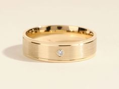 a yellow gold wedding ring with a diamond in the center, on a white background