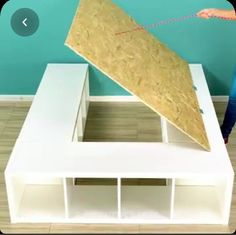 a person is holding a piece of plywood on top of a white table with shelving underneath it