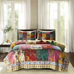 a bed with colorful bedspread and pillows on top of it next to a window