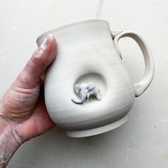 a hand holding a white vase with an elephant in it's hole on the side