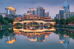 a bridge over a body of water in front of tall buildings with lights on them