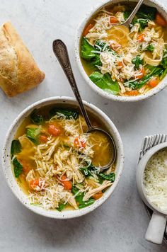 two bowls of chicken noodle soup on a white surface with bread and spoons