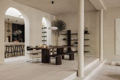 a dining room with white walls and flooring next to an open kitchen area that also has bar stools