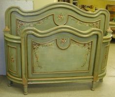 an antique green painted bed frame with flowers and scrolls on the headboard, sitting in a room