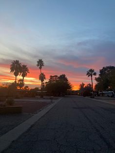 the sun is setting behind palm trees in this street scene with cars parked on both sides