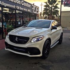 a white mercedes suv is parked in front of a building with an advertisement on it