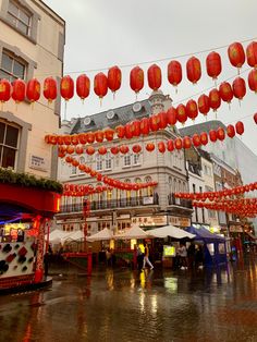 many red lanterns are hanging from the ceiling in front of buildings and umbrellas on a rainy day