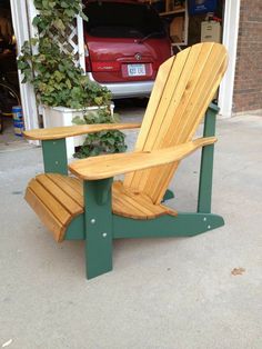 a wooden adiron chair sitting in front of a garage with a red car parked behind it