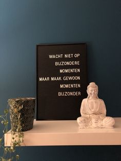 a buddha statue sitting on top of a white shelf next to a black framed sign