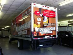 a delivery truck parked in a garage with advertisements on the side of it's back