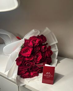 a bouquet of red roses sitting on top of a white table next to a card