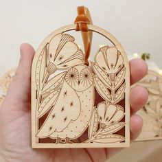 a hand holding a wooden ornament with an owl and flowers design on it