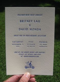 a hand holding up a wedding card in front of the camera, with an image of a bicyclist on it