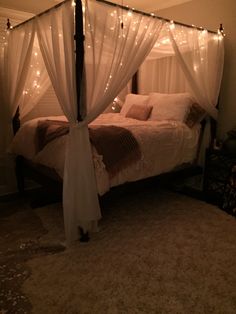 a canopy bed with white curtains and lights on the headboard is lit up at night