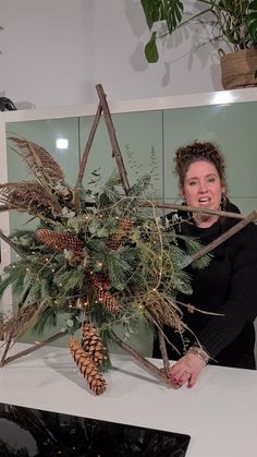 a woman standing behind a table with pine cones and branches