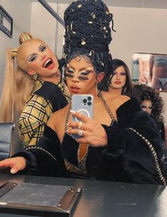 two women dressed in costumes taking a selfie with a cell phone at a table