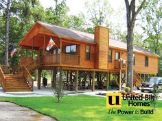 a large wooden house sitting in the middle of a lush green field with stairs leading up to it