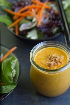 a glass jar filled with yellow liquid next to a salad