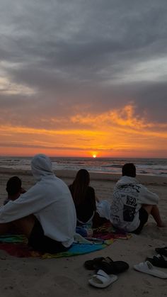 three people sitting on the beach watching the sun set