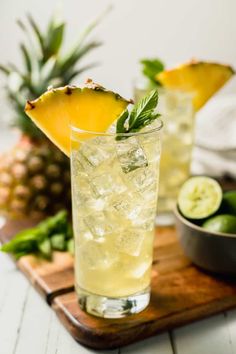 two glasses filled with lemonade and limes on top of a wooden cutting board