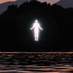 a person standing in the water with their arms spread out to the side at night