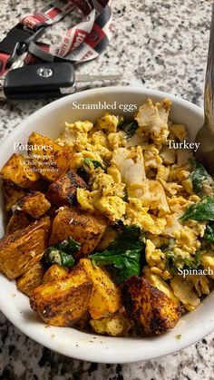 a bowl filled with scrambled eggs, potatoes, spinach and spinach leaves next to a pair of scissors