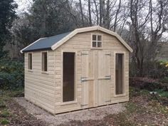 a small wooden shed sitting in the middle of a field with trees and bushes behind it