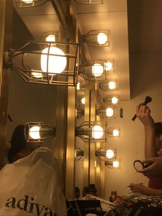 a woman is brushing her teeth in front of a mirror with lights on the ceiling